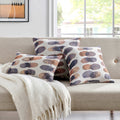 A trio of Vibrant Brightside Pillows placed on a beige sofa, offering a cozy and stylish addition to any living space with their unique blue and brown circular designs.